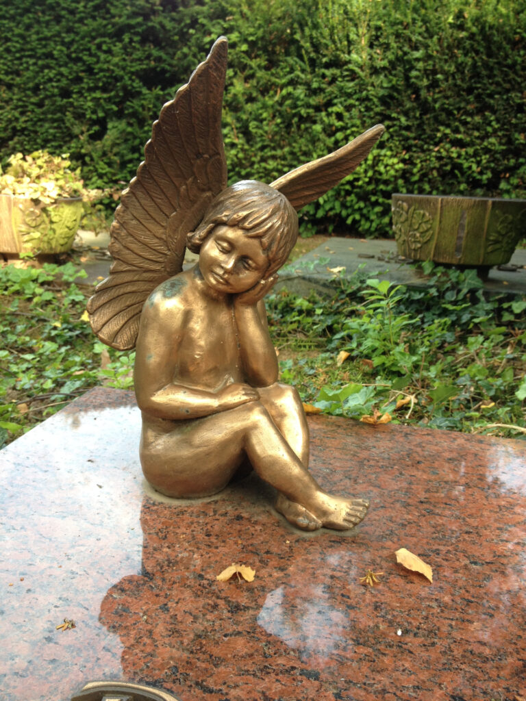 Goldener Engel sitzt schlafend auf einer Grabplatte