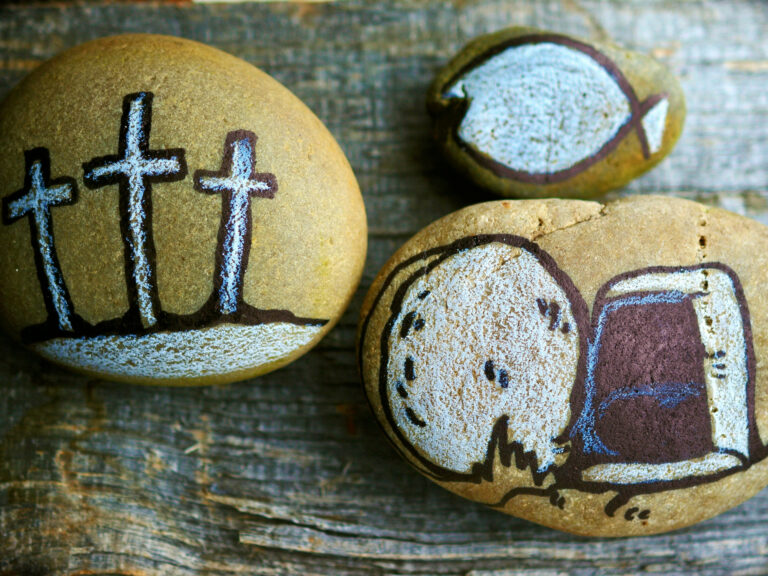 Steine, die bemalt sind mit drei Kreuzen, dem geöffneten Grab Jesu und einem Fisch (Ichthys)